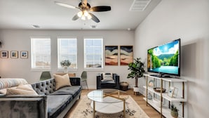 Een moderne woonkamer met een bank, fauteuil, salontafel, televisie en decoratieve objecten.