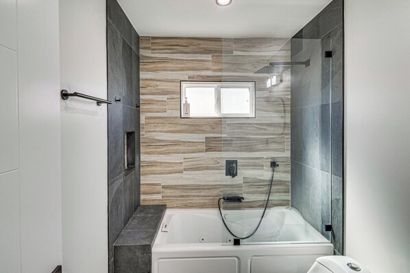 A modern bathroom with a bathtub, a shower, and a window.