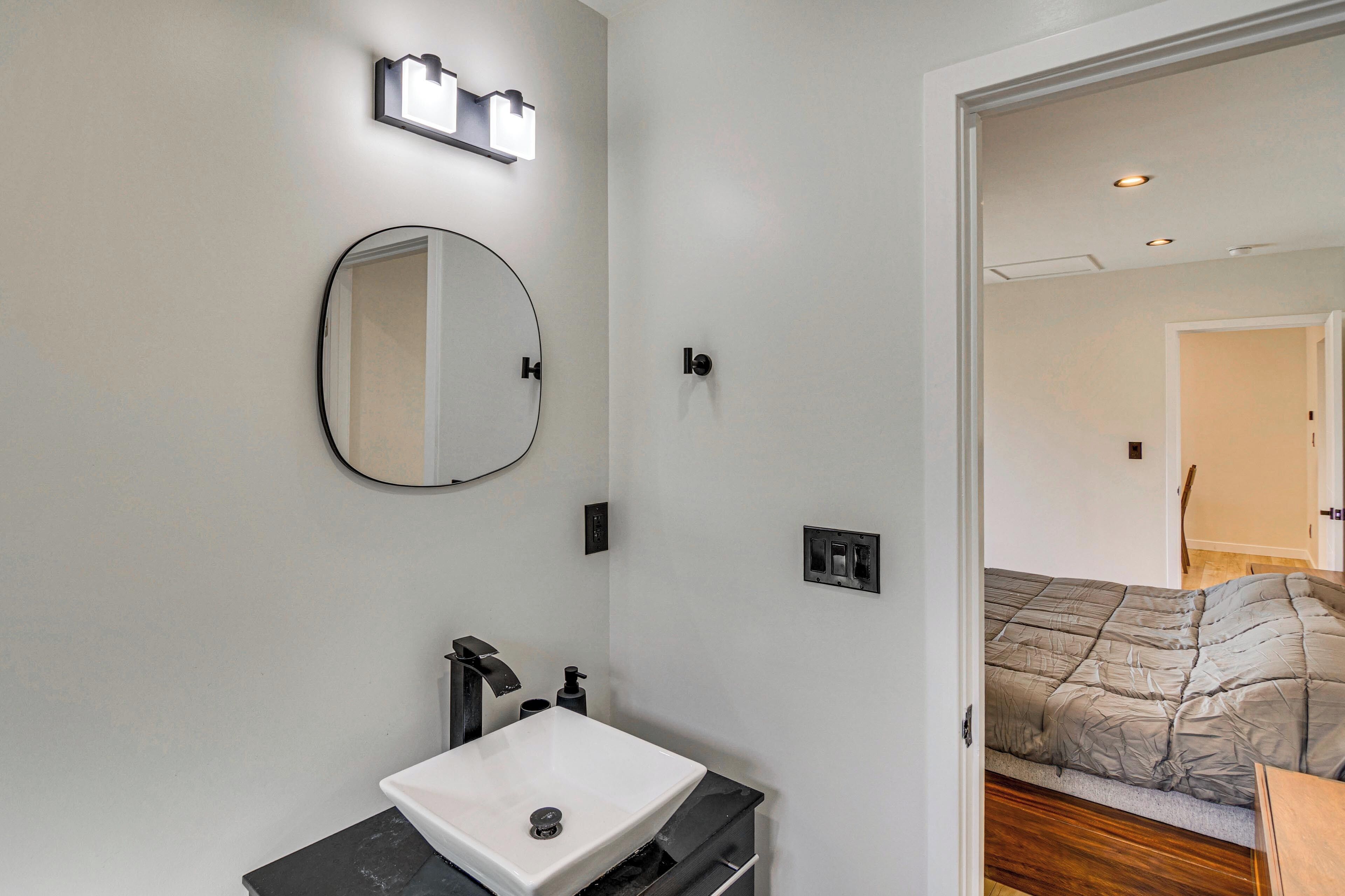 A bathroom with a white sink, a round mirror, and a black countertop.