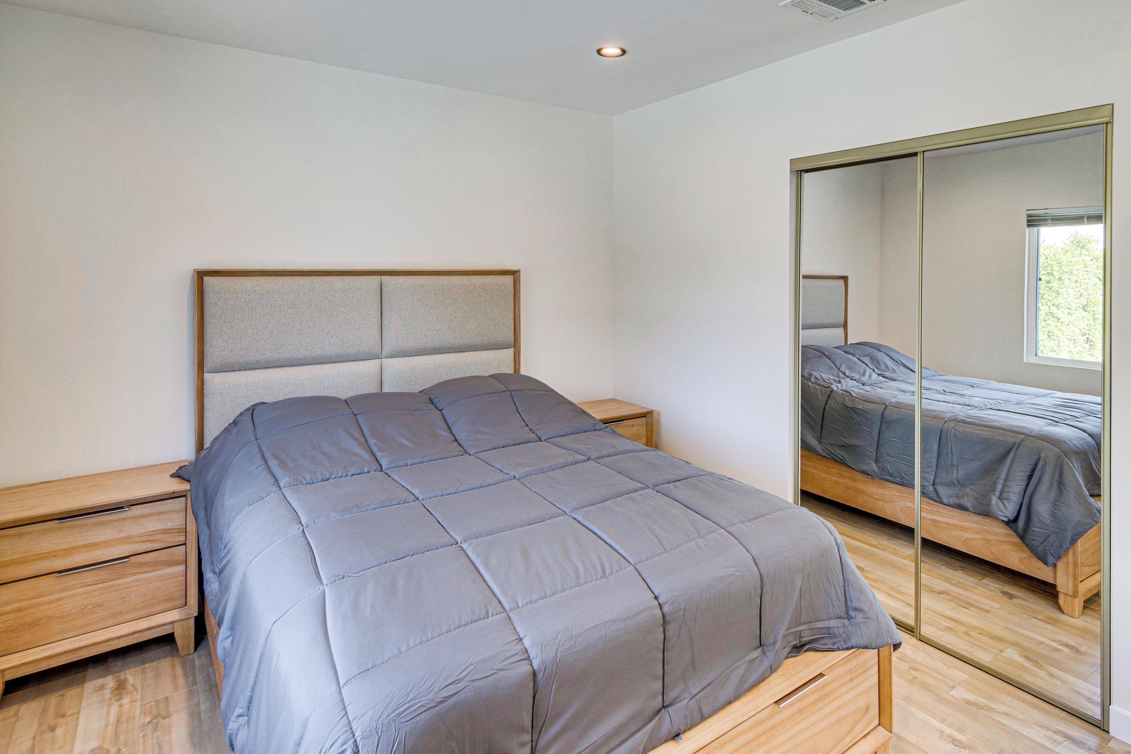 A modern bedroom with a bed, bedside tables, a mirror, and a window.