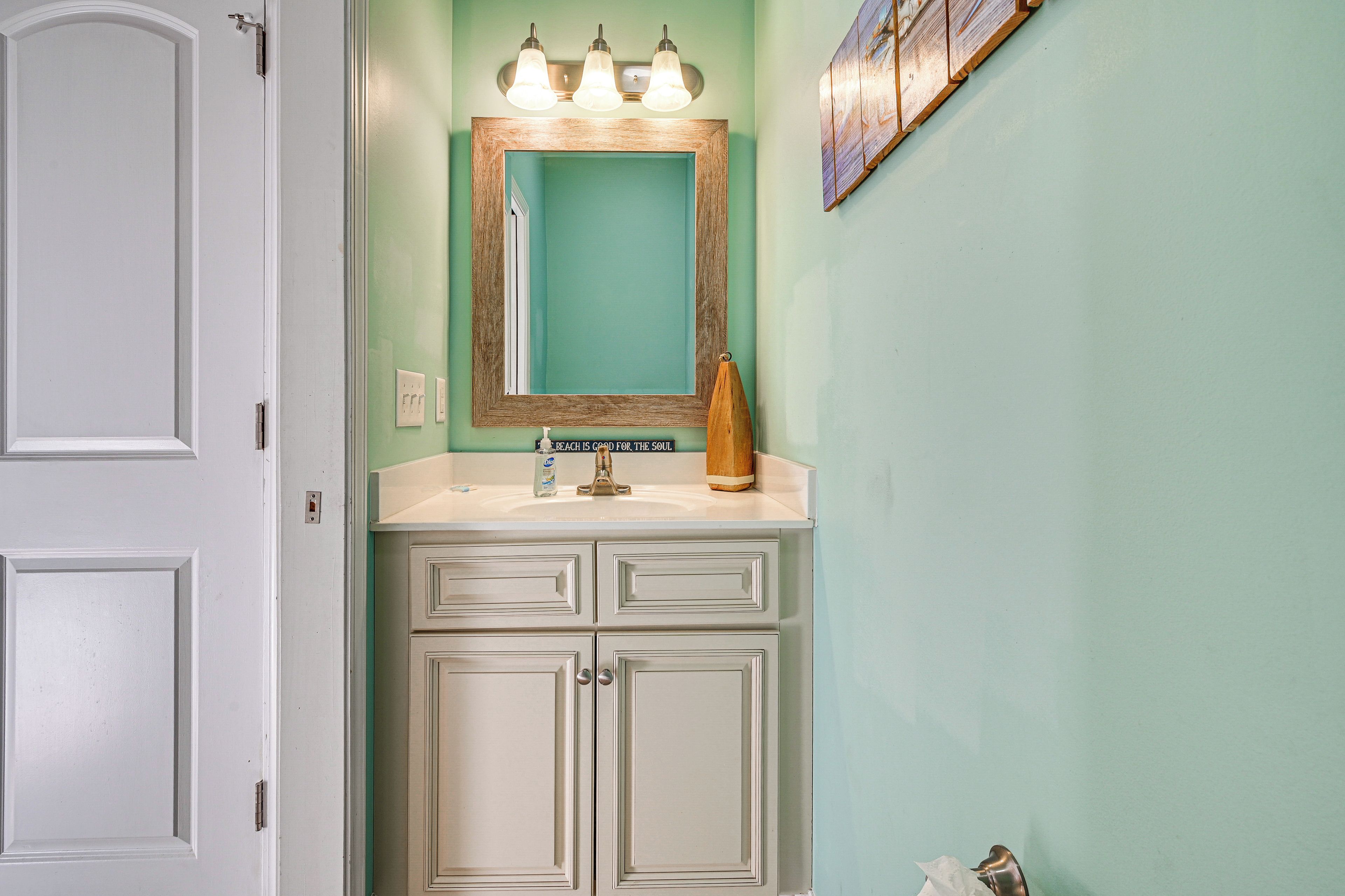 Une salle de bain avec un meuble-lavabo blanc, un miroir avec un cadre en bois et un luminaire placé au-dessus du miroir.