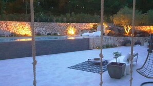 An outdoor patio with a stone wall, lounge chairs, a hammock, and a fire pit. - Villa Maluan (Mons)