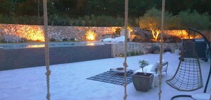 Eine Außenpatio mit Steinmauer, Liegestühlen, einer Hängematte und einem Feuerkorb.