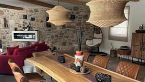 A dining area with a long wooden table, brown leather chairs, woven pendant lights, and a stone wall backdrop. - Villa Maluan (Mons)