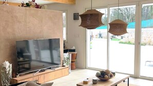 A modern living room with a large flat-screen TV, a wooden ceiling, and a large window. - Villa Maluan (Mons)