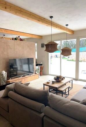 Ein modernes Wohnzimmer mit einem großen Flachbildfernseher, einer Holzbalkendecke und einem großen Fenster.