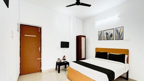 A bedroom with a bed, a wooden wardrobe, a small table with a kettle, a television, and artwork on the wall. - Deluxe Vinayak Residency Patravakam Inn (Chennai)