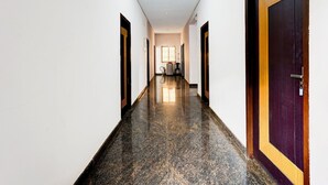 A hallway with a polished floor, white walls, and doors with a dark wood finish and a yellow stripe. - Deluxe Vinayak Residency Patravakam Inn (Chennai)