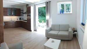 Una sala moderna con un sofá, una mesa de centro y vistas a una cocina con armarios de madera y un ventanal.