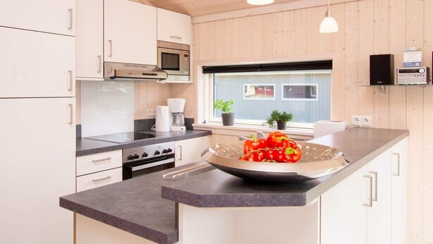 A modern kitchen with wooden cabinets, a microwave, stove, and a large island with a bowl of tomatoes. - 4 Star Holiday Home in Grossenbrode (Grossenbrode)
