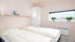 A bedroom with two beds, a window with plants, a radiator, and a white wardrobe. - 4 Star Holiday Home in Grossenbrode (Grossenbrode)