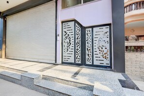 A closed metal garage door, a set of steps leading to a building entrance, and a decorative gate with geometric patterns. - Deluxe Collection O Sadar Bazaar (Gurugram)