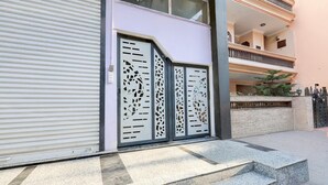 A building with a closed shutter door, a set of steps leading to a gated entrance, and a multi-story structure with balconies. - Super Collection O Sadar Bazar Gurgaon (Gurugram)