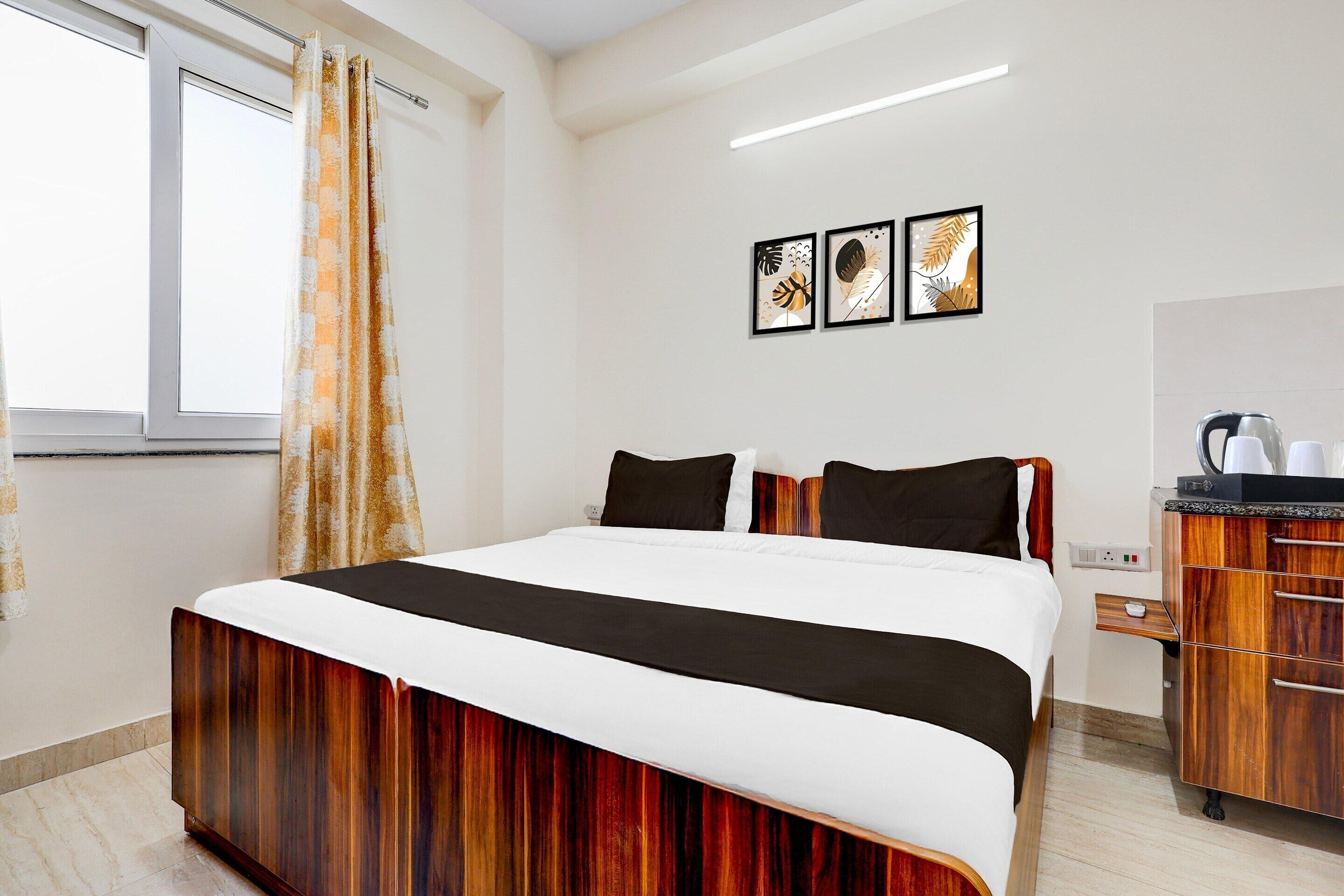 A hotel room with a bed, a wooden dresser, and two framed pictures on the wall.