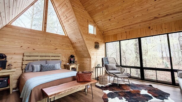 Ein gemütliches Schlafzimmer in einer Blockhütte mit einem Bett, einem Sessel, einem großen Fenster und einem Deckenventilator.