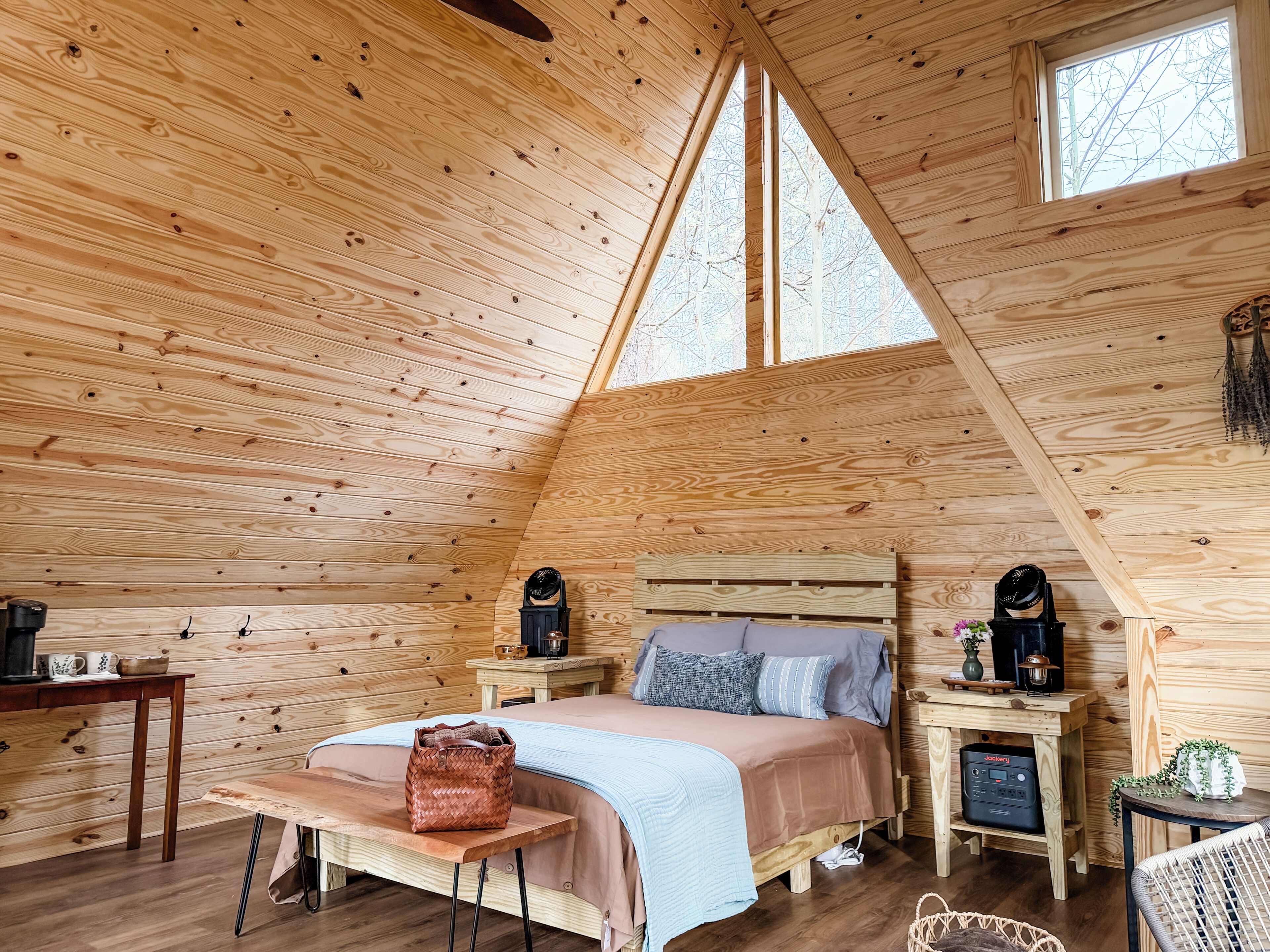 A wooden cabin bedroom with a bed, bedside tables, a desk, and a window.