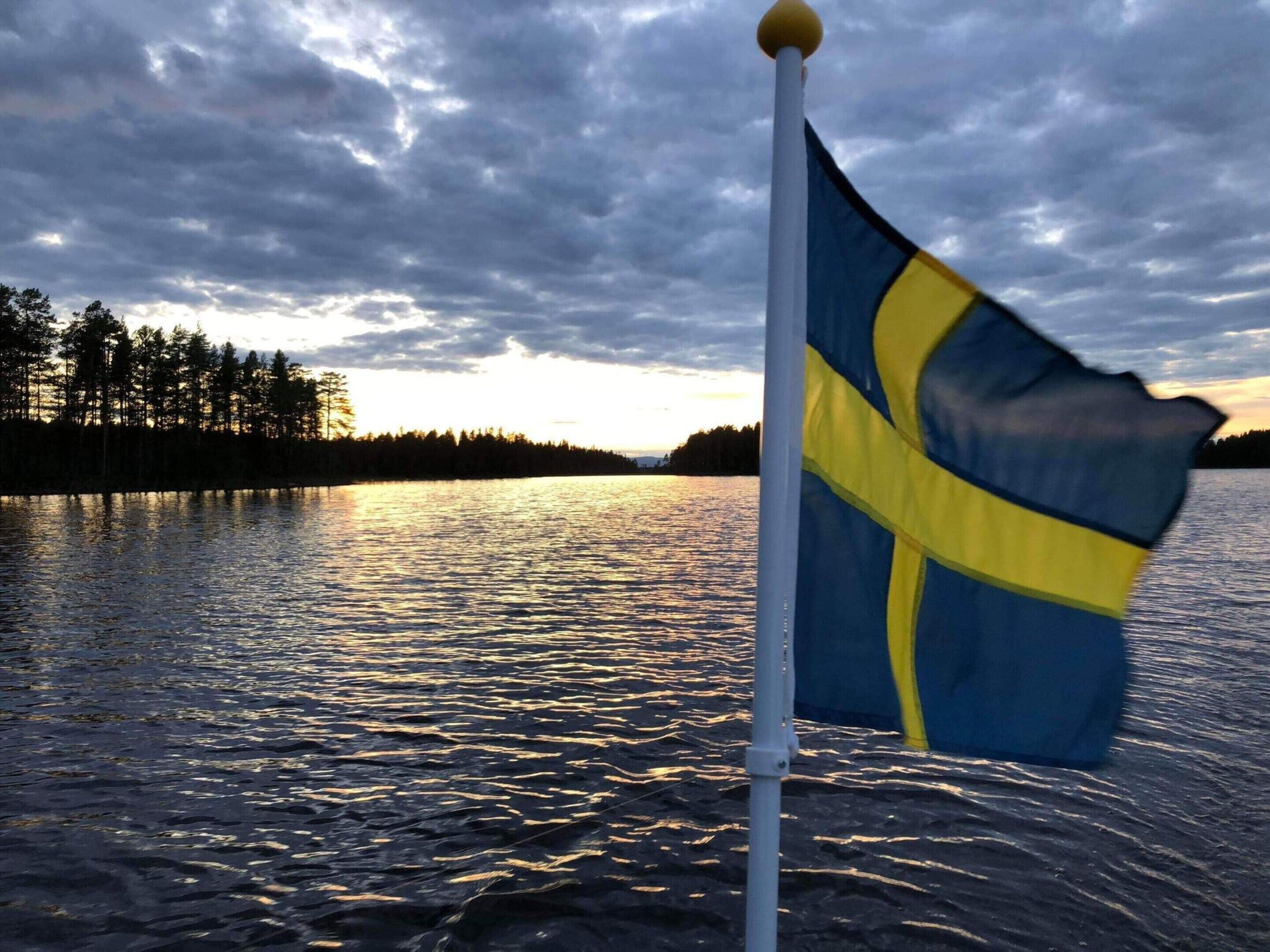 Un mât sur lequel flotte un drapeau, une étendue d’eau et une rive bordée d’arbres.