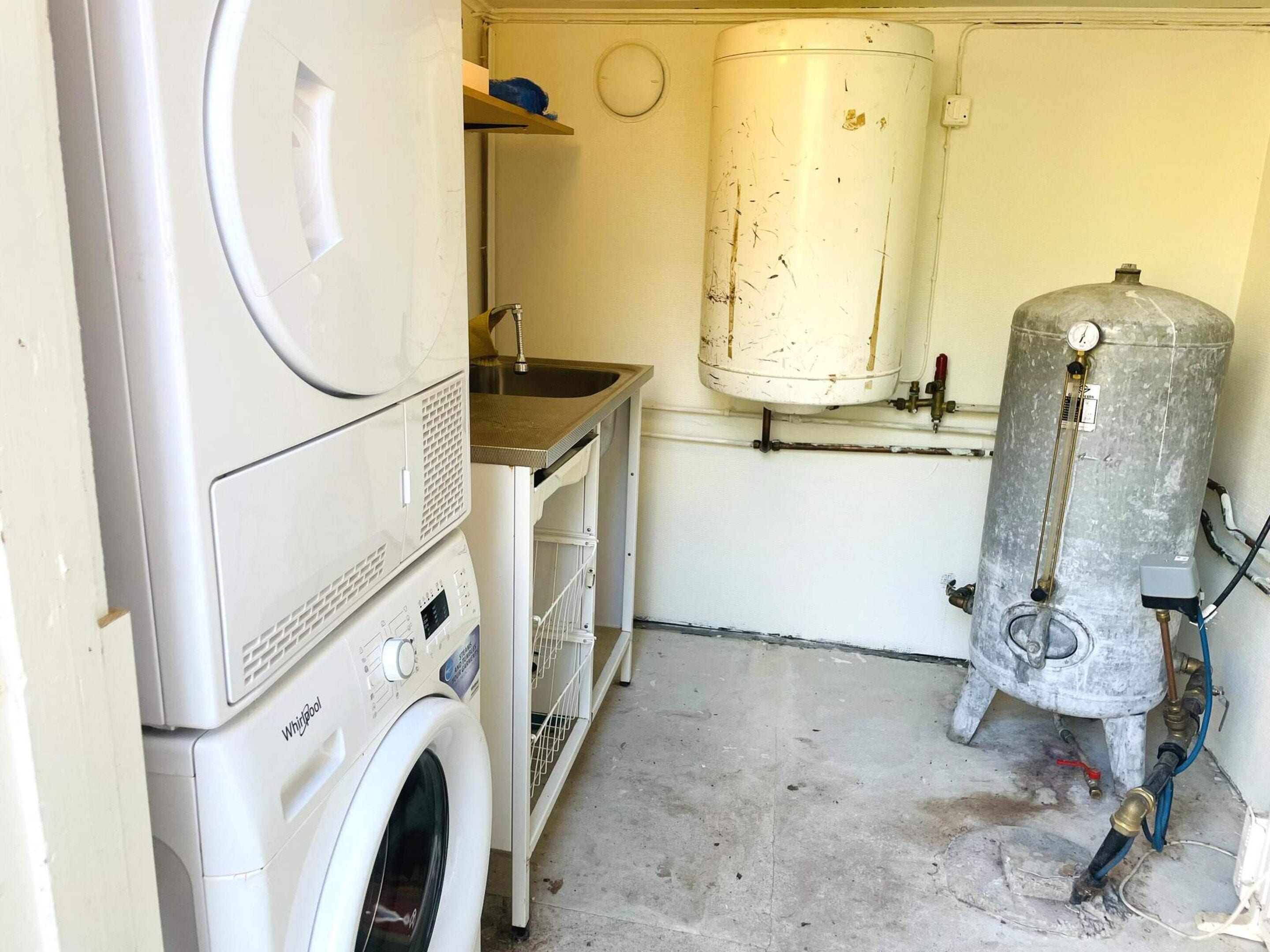 Un área de lavandería con lavadora, lavabo y calentador de agua.