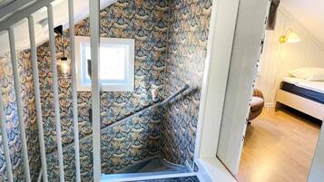 Una escalera con pared de piedra, barandilla blanca y una cama en la habitación contigua.