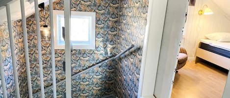 A staircase with a stone wall, a white railing, and a bed in the adjacent room.