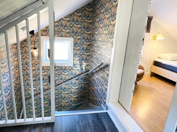 Una escalera con pared de piedra, barandilla blanca y una cama en la habitación contigua.
