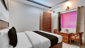 A hotel room with a bed, a desk, a chair, a wardrobe, and a window with curtains.