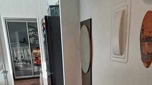 Ein Flur mit Holzboden, einem schwarzen Hocker, einem Spiegel und einer Tür, die in einen Raum mit einem Fenster zu einem Gebäude führt.