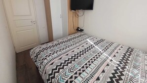 Ein Zimmer mit einem Bett, einem an der Wand befestigten Fernseher und einem Kleiderschrank.