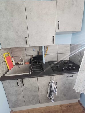A kitchen with grey cabinets, a black countertop, a sink, a stove, and a towel hanging. - Rakvere 32  apartment  on second floor near the border  (Narva)