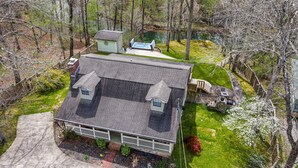 A house with a sloped roof, a fenced yard, and a small pond. - Drop A Line – Riverfront Relaxation on Little Riverer (Mentone)