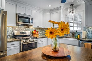 A modern kitchen with white cabinets, stainless steel appliances, a wooden dining table, and a vase with sunflowers.