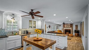 A spacious kitchen with white cabinets, a wooden island, and a ceiling fan. - Drop A Line – Riverfront Relaxation on Little Riverer (Mentone)