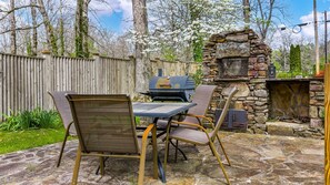 An outdoor patio with a stone table, two chairs, a grill, and a stone fireplace. - Drop A Line – Riverfront Relaxation on Little Riverer (Mentone)