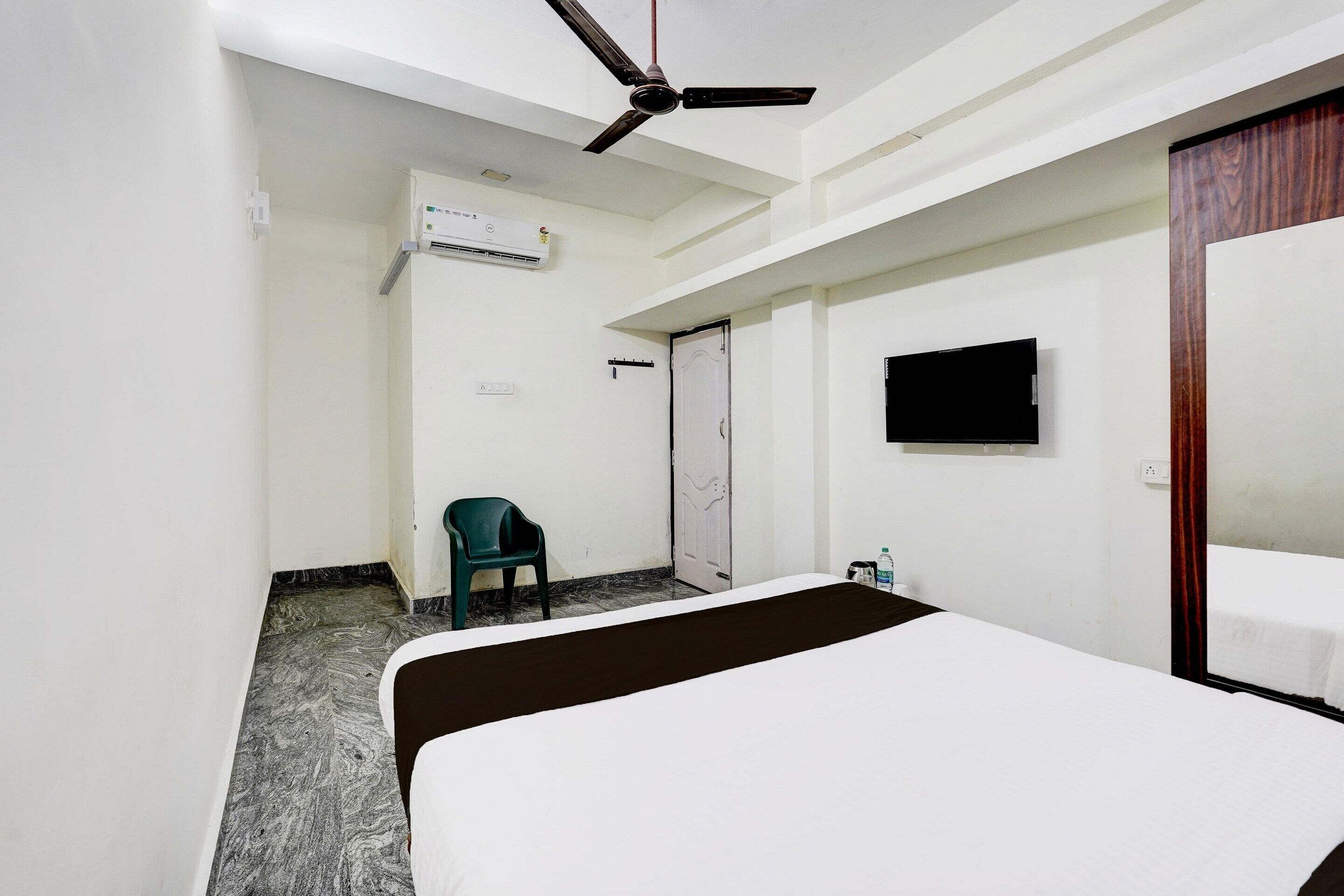 Een hotelkamer met een bed, een plafondventilator, een airconditioning, een televisie en een deur.