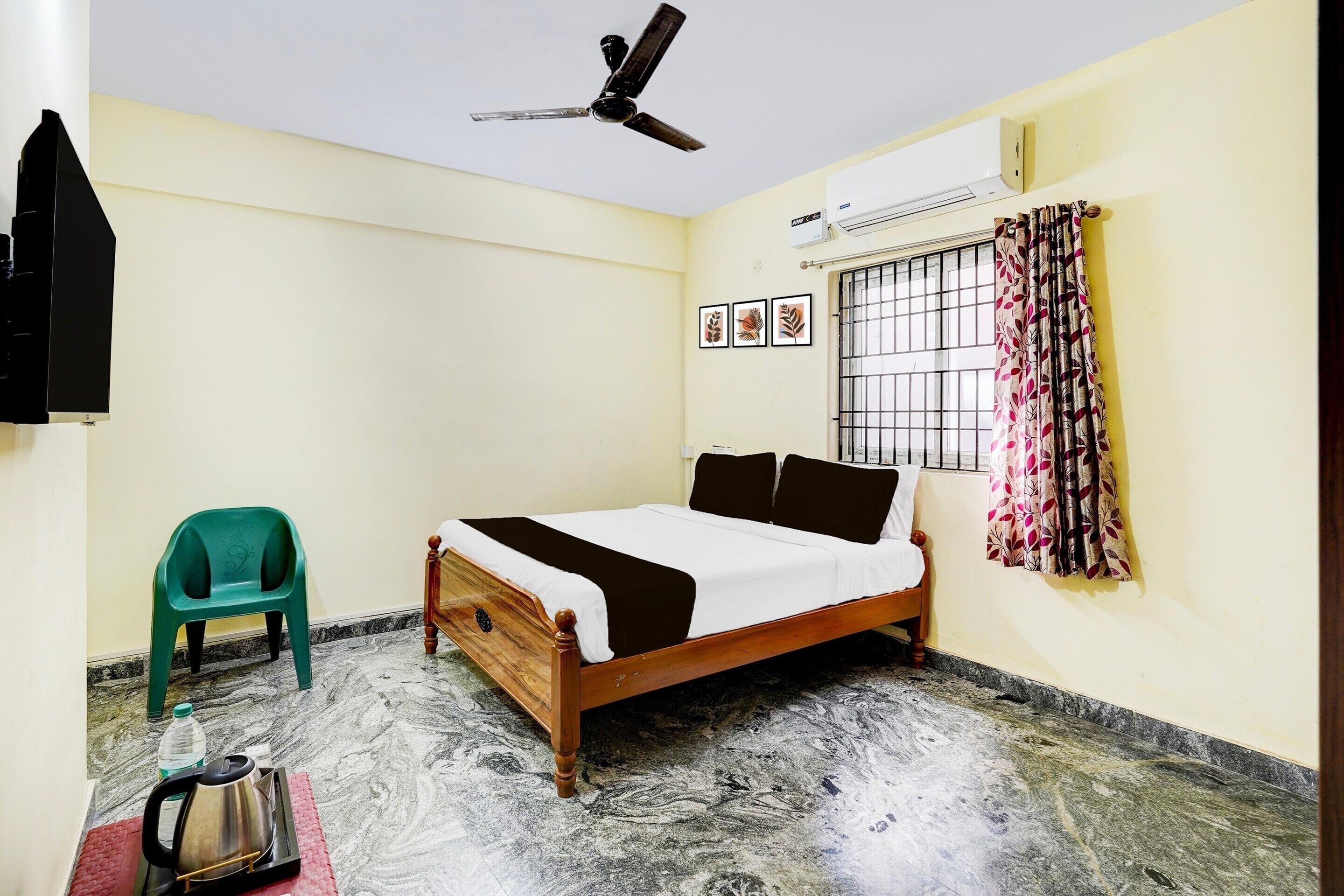 A bedroom with a bed, a ceiling fan, an air conditioning unit, a window with bars, and a green plastic chair.