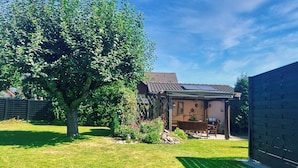 A house with a covered patio, a tree, and a fenced yard. - Apartment Glückliche Zeit 100sqm in the basement with billiard room & garden with terrace (Osterode am Harz)