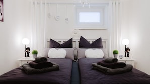 A bedroom with a double bed, two bedside tables with lamps, a window with blinds, and a chandelier. - Apartment Glückliche Zeit 100sqm in the basement with billiard room & garden with terrace (Osterode am Harz)