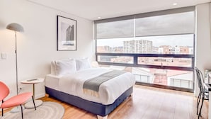 Ein modernes Schlafzimmer mit großem Fenster, einem Bett, einem Schreibtisch und einem Sessel.