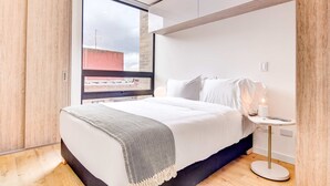 Ein modernes Schlafzimmer mit großem Fenster, einem Bett mit weißer Bettwäsche, einem Nachttisch mit Lampe und Holzboden.