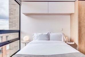 Ein modernes Hotelzimmer mit einem großen Bett, einem Nachttisch mit Lampe, Blick auf die Stadt durch ein Fenster und einer Wand mit Holzvertäfelung.