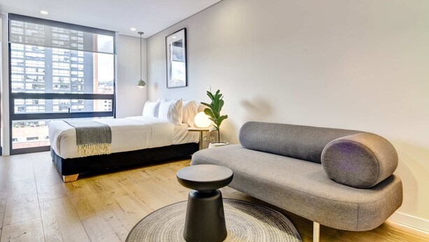 A modern bedroom with a large window, a bed, a grey sofa, and a small round table. - w Signature Loft in the Heart of Bogot (Bogotá)