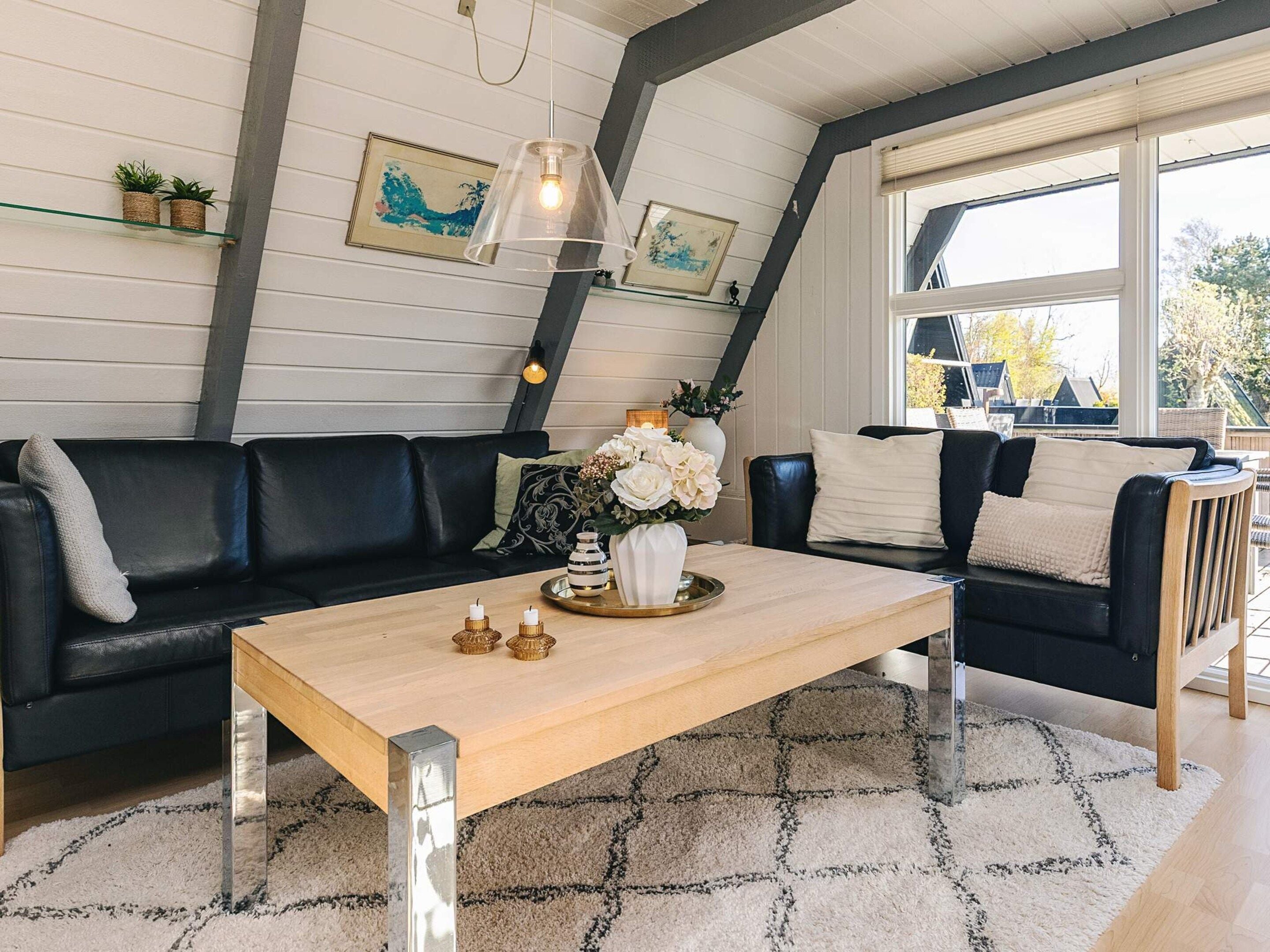 A modern living room with a black leather sofa, a wooden coffee table, and a large window providing a view of the outdoors.