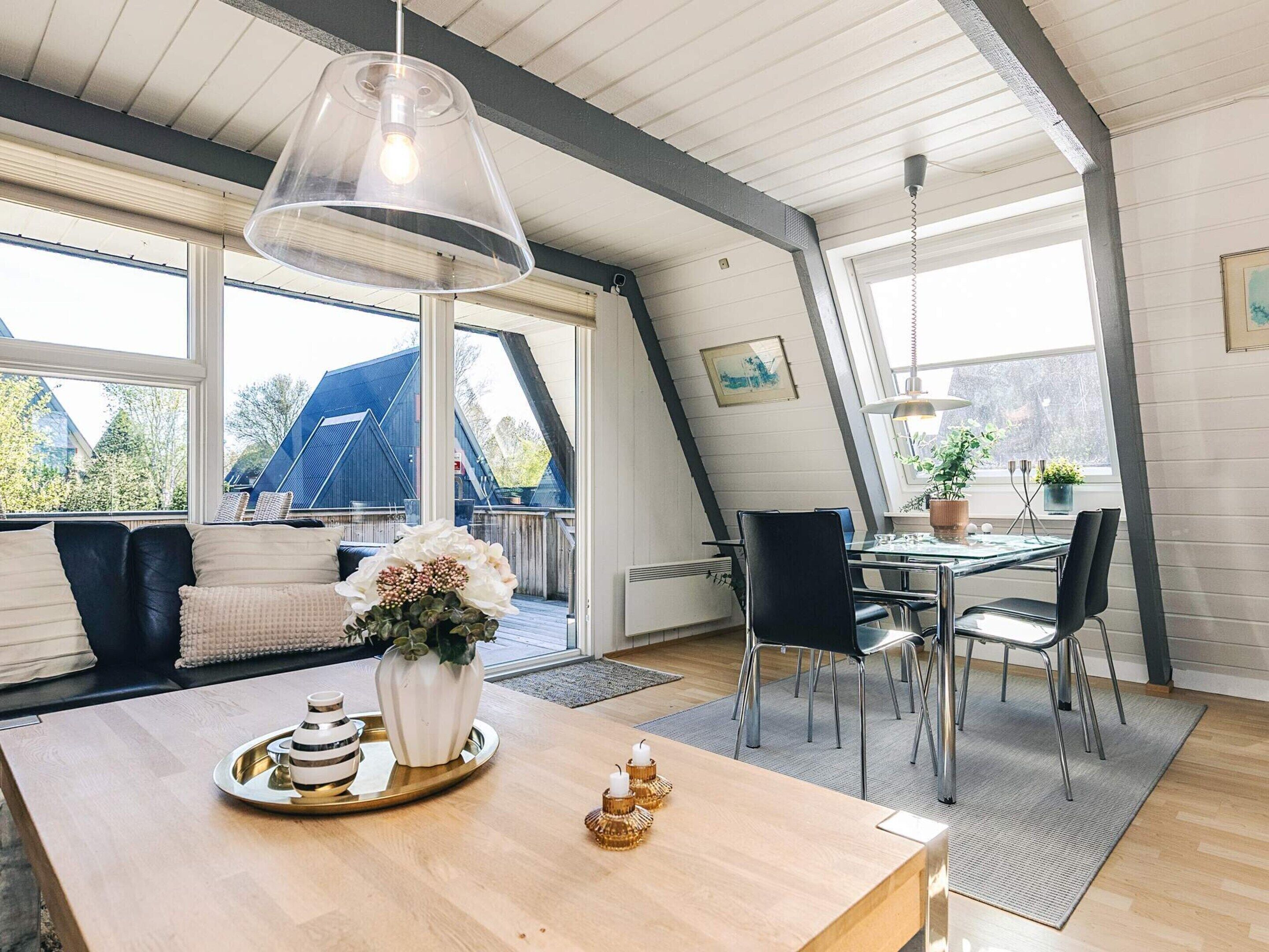 A modern interior with a dining area, a sofa with cushions, a table with a lamp, and a view of the outside.