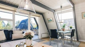 A modern interior with a dining area, a sofa with cushions, a table with a lamp, and a view of the outside. - 4 Star Holiday Home in Farso (Farso)