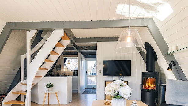 A modern loft with a kitchen, dining area, and living room, featuring a staircase, TV, fireplace, and a view of the outdoors. - 4 Star Holiday Home in Farso (Farso)