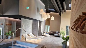 A modern indoor pool area with a glass wall, lounge chairs, and a seating area with a sofa and table. - 4 Star Holiday Home in Farso (Farso)