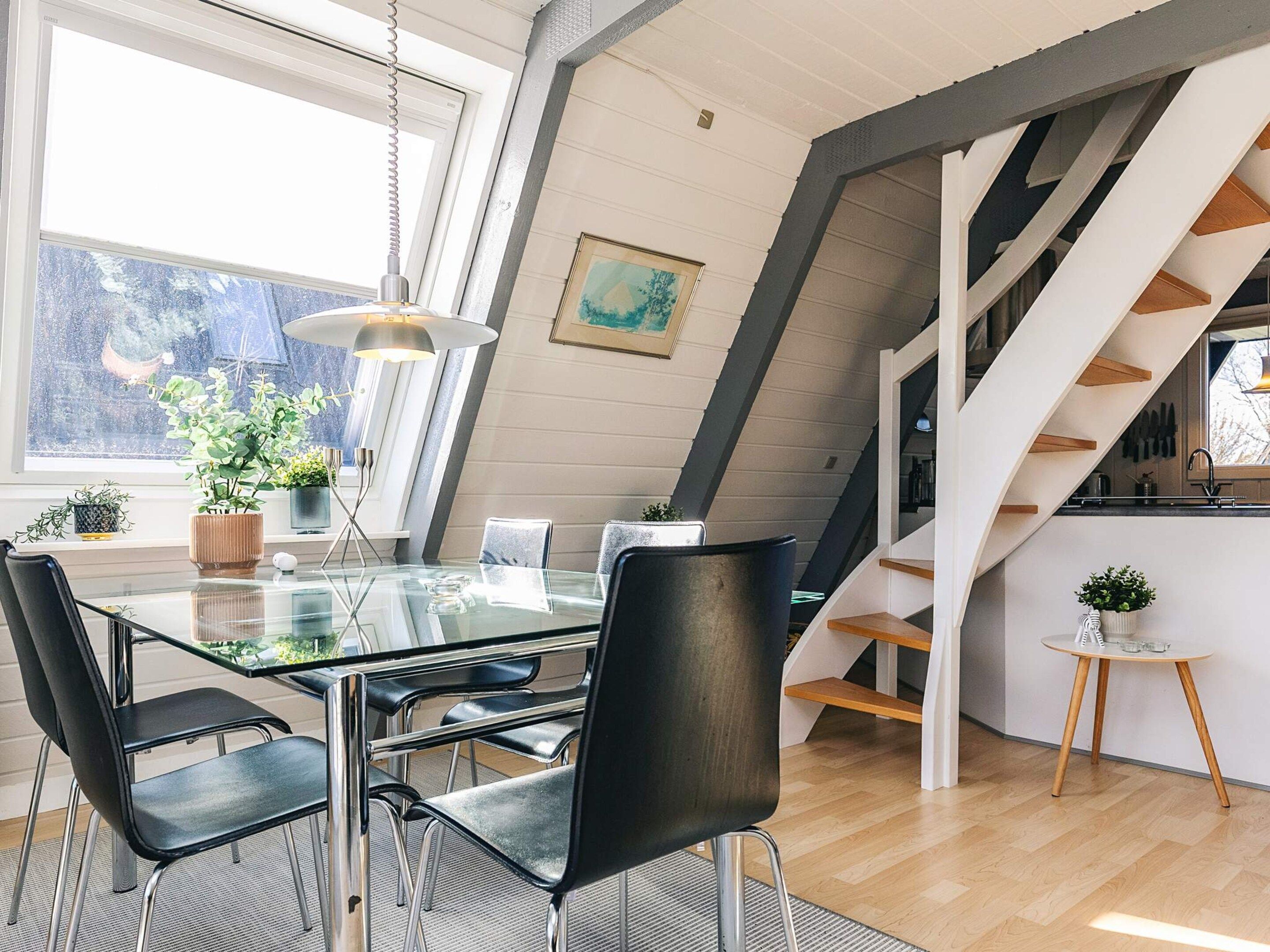Een modern interieur met een glazen eettafel, zwarte stoelen, een hanglamp en een trap met houten treden.