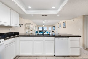 A kitchen with white cabinets, a black countertop, and a dishwasher. - Wake Up to Ocean Views - Beachfront Balcony Pool (South Padre Island)
