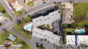 Vista aérea de un edificio comercial con estacionamiento, piscina y zonas ajardinadas.