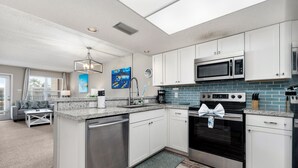 Una cocina moderna con armarios blancos, un lavavajillas de acero inoxidable, un horno negro con diseño arqueado, un microondas y un salpicadero de azulejos azules.